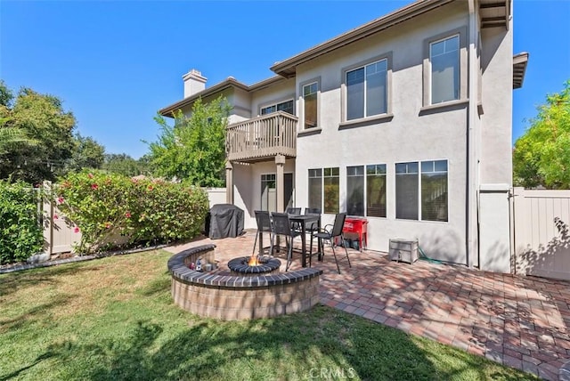 back of house with a balcony, a yard, stucco siding, a chimney, and an outdoor fire pit