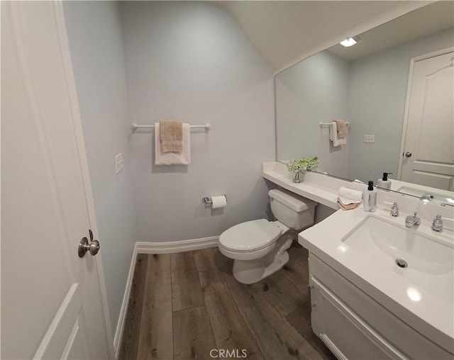 half bath with vanity, toilet, wood finished floors, and baseboards