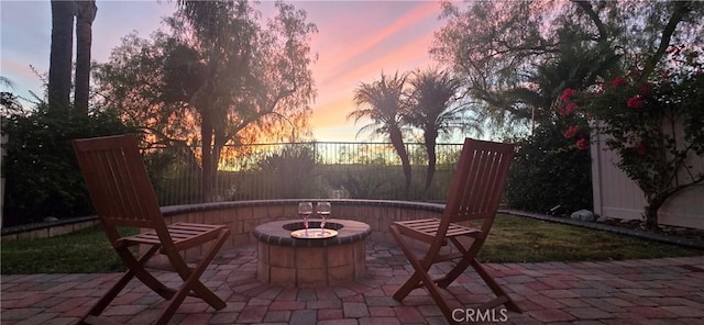 patio terrace at dusk featuring a fire pit and fence