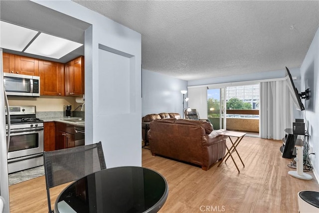 interior space featuring appliances with stainless steel finishes, light wood finished floors, light countertops, brown cabinetry, and open floor plan