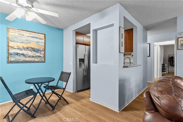 interior space featuring brown cabinetry, a textured ceiling, stainless steel fridge with ice dispenser, a ceiling fan, and light wood finished floors