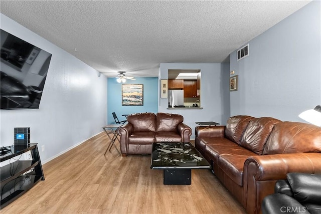 living area with ceiling fan, a textured ceiling, visible vents, wood finished floors, and baseboards