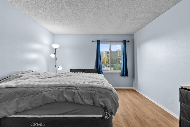 bedroom with baseboards, light wood finished floors, and a textured ceiling