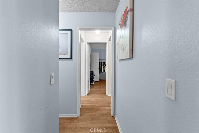 hall with baseboards, a textured wall, and wood finished floors