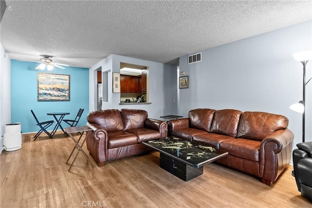 living area featuring a textured ceiling, ceiling fan, visible vents, and light wood-style flooring