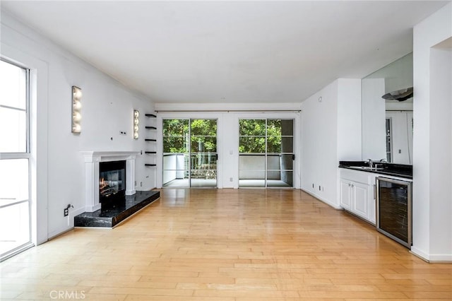 unfurnished living room with a glass covered fireplace, light wood-style flooring, beverage cooler, and a sink