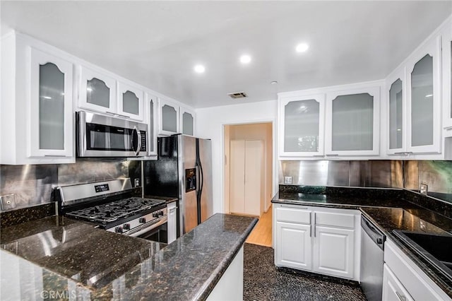 kitchen with white cabinets, stainless steel appliances, dark stone countertops, and tasteful backsplash