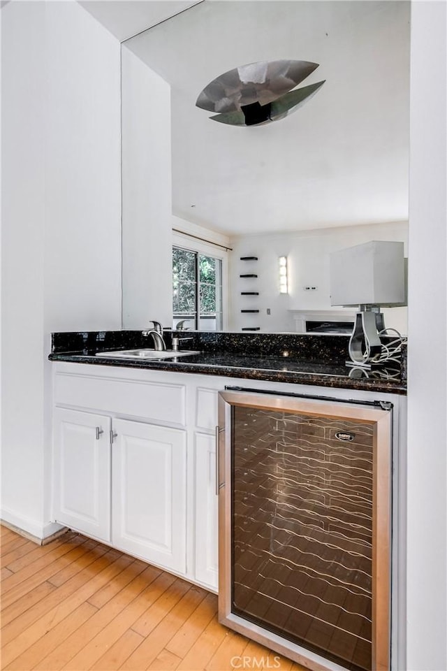kitchen featuring wine cooler, light wood-style flooring, white cabinetry, a sink, and dark stone countertops