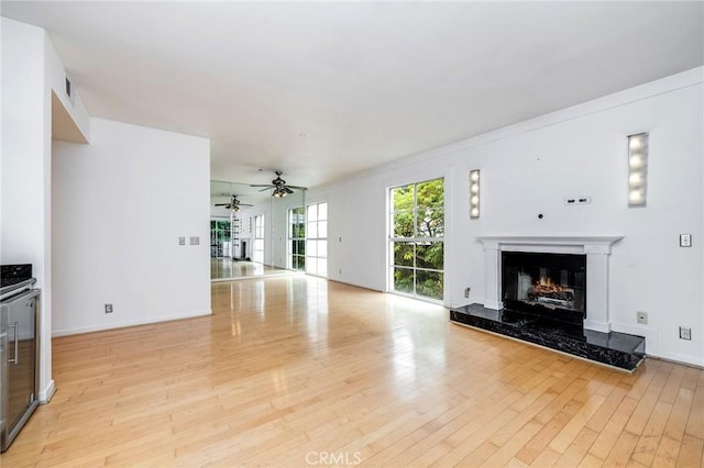 unfurnished living room featuring light wood-style floors, a ceiling fan, baseboards, and a fireplace