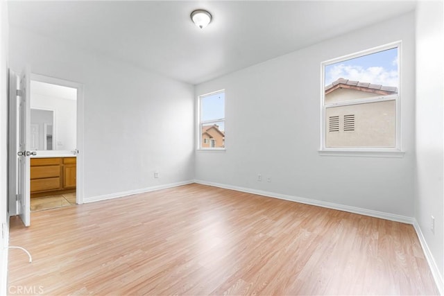 unfurnished bedroom featuring light wood-style floors, baseboards, and connected bathroom