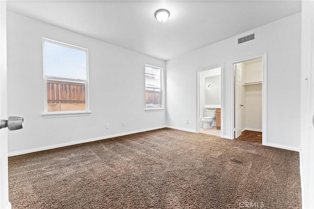 unfurnished bedroom with visible vents, baseboards, ensuite bathroom, a walk in closet, and carpet