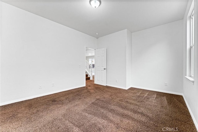 unfurnished room with dark carpet and baseboards