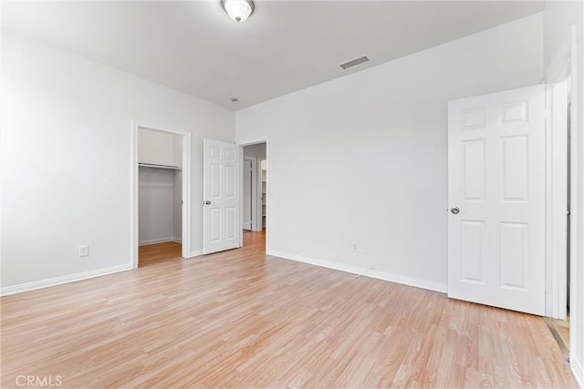 unfurnished bedroom with visible vents, a closet, light wood-style floors, baseboards, and a walk in closet