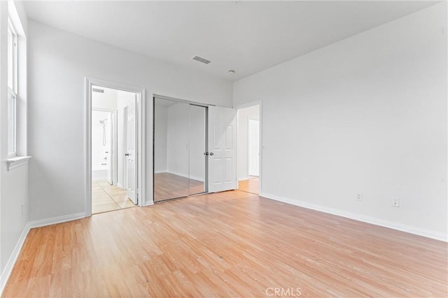 unfurnished bedroom with visible vents, a closet, baseboards, light wood-style flooring, and ensuite bath