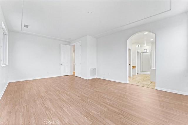 empty room with baseboards, arched walkways, light wood-style flooring, and visible vents