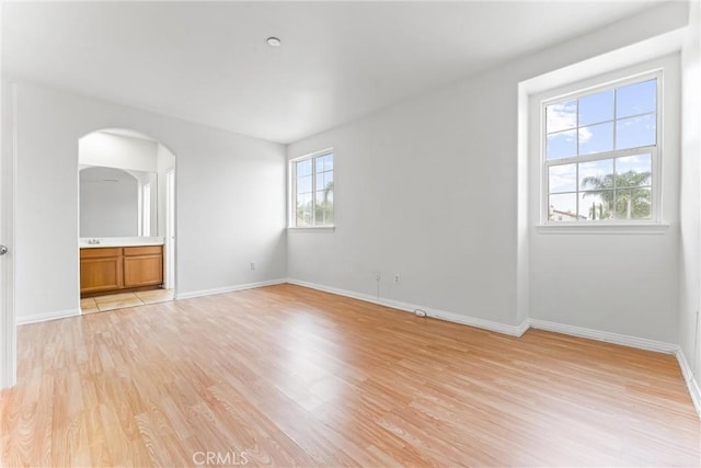 unfurnished living room featuring light wood-style floors, arched walkways, and baseboards