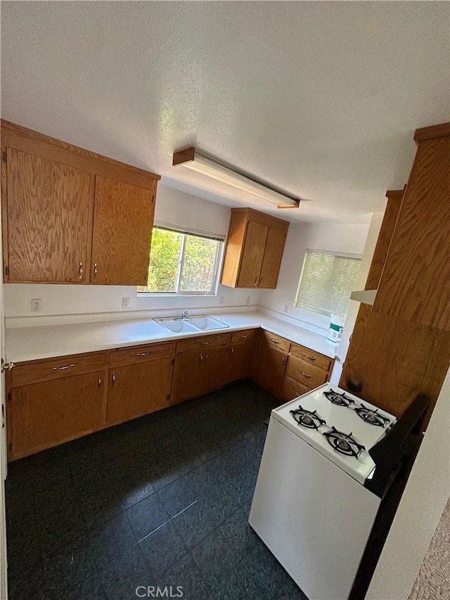 kitchen featuring a sink, light countertops, brown cabinetry, and white range with gas cooktop