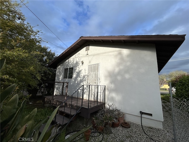 view of side of home featuring fence, stucco siding, and a deck