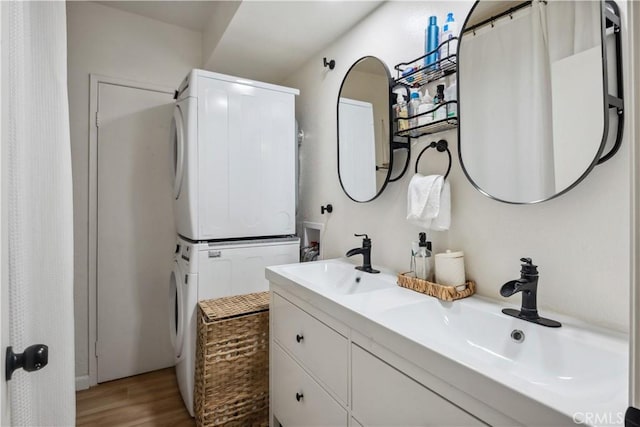 full bath featuring a sink, double vanity, stacked washer / drying machine, and wood finished floors