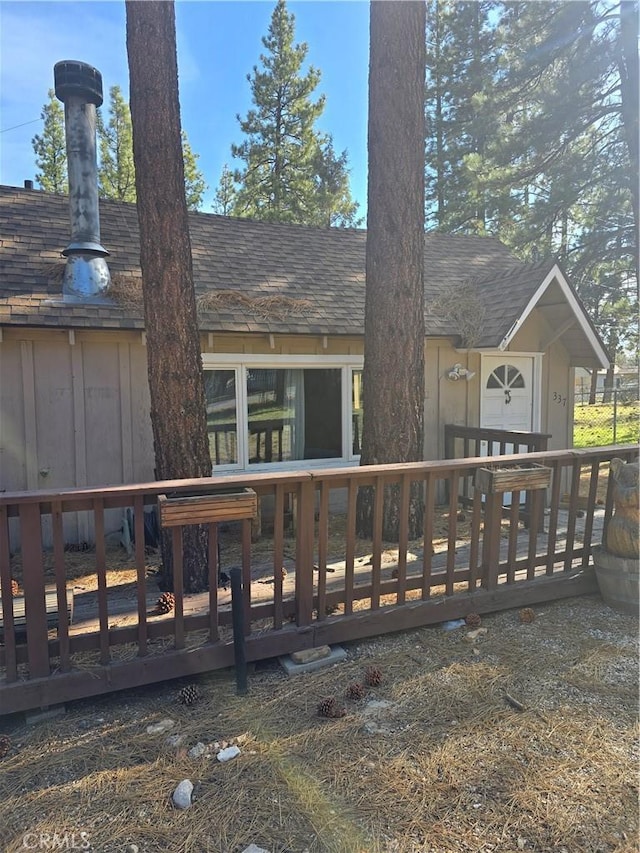 back of house featuring roof with shingles and a wooden deck
