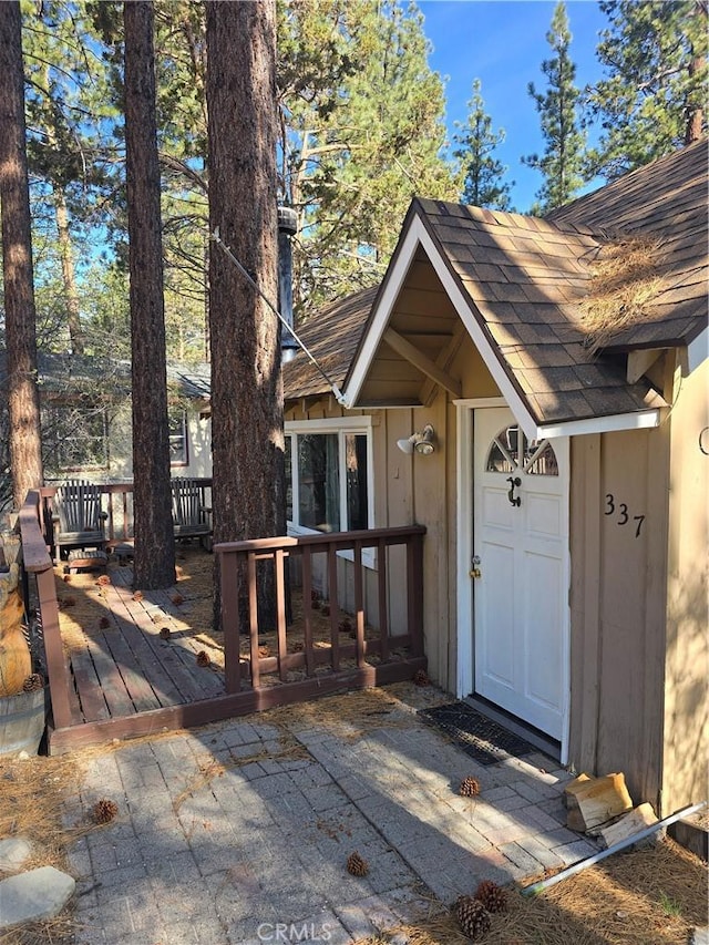 view of exterior entry featuring a shingled roof and a deck