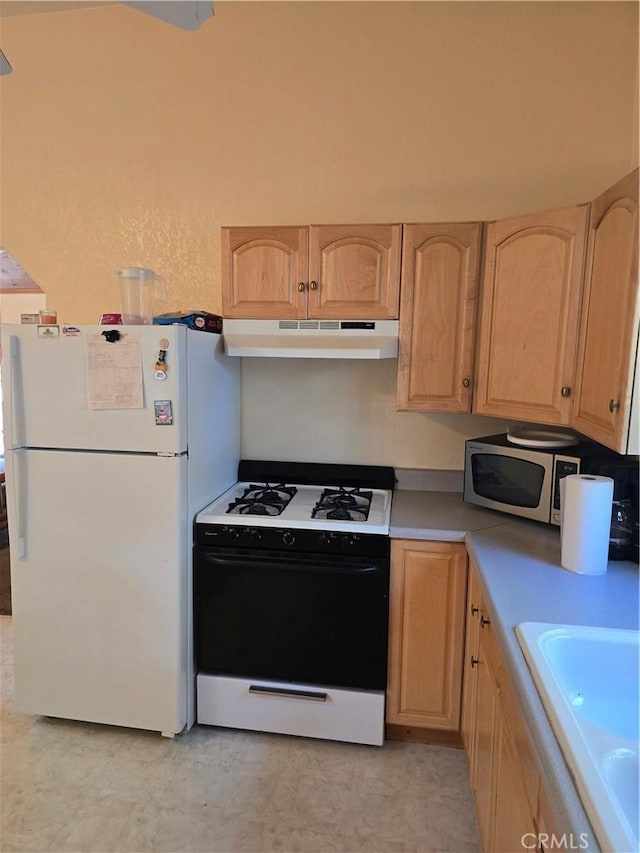 kitchen featuring freestanding refrigerator, light brown cabinets, gas range, stainless steel microwave, and under cabinet range hood