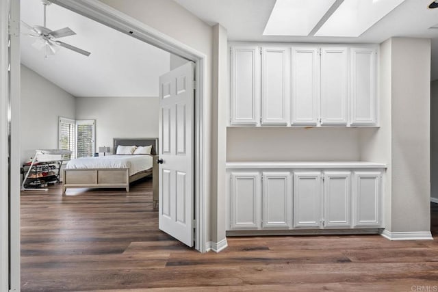 bedroom with baseboards, vaulted ceiling with skylight, and dark wood-style floors