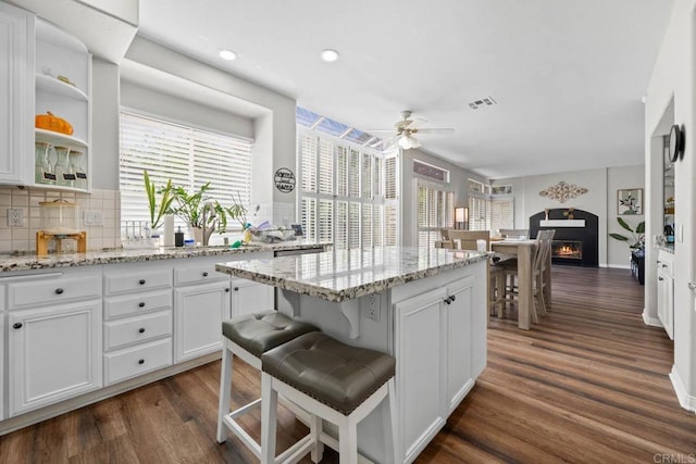 kitchen with dark wood-style flooring, a center island, a ceiling fan, white cabinetry, and visible vents