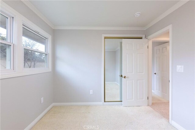 unfurnished bedroom featuring carpet flooring, ornamental molding, baseboards, and a closet