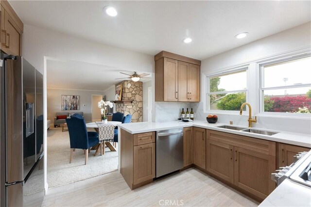 kitchen with appliances with stainless steel finishes, a sink, a peninsula, open floor plan, and light countertops