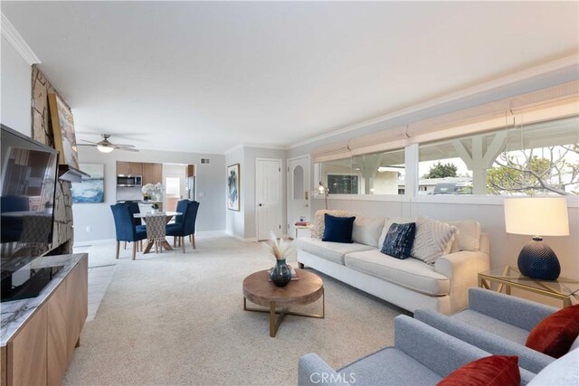 living room featuring light carpet, ornamental molding, baseboards, and ceiling fan
