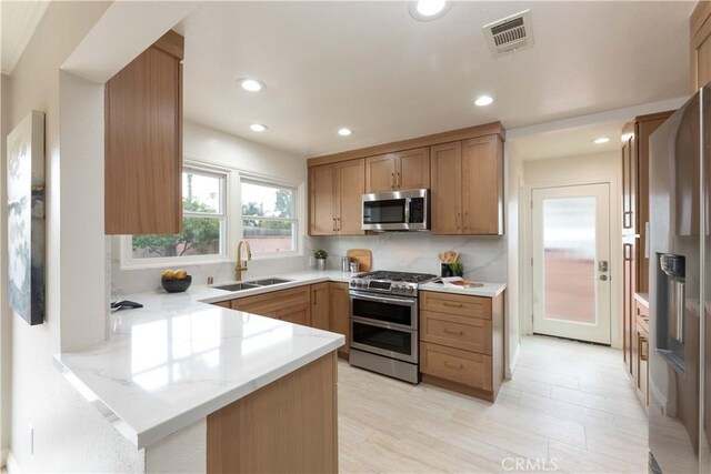 kitchen with appliances with stainless steel finishes, a sink, a peninsula, light stone counters, and recessed lighting