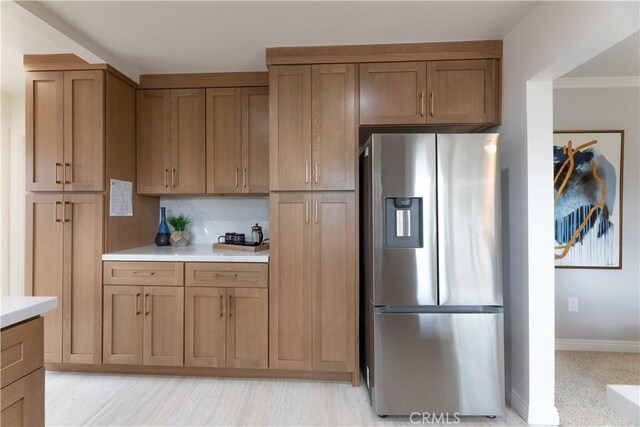 kitchen with stainless steel fridge with ice dispenser, light countertops, baseboards, brown cabinetry, and crown molding