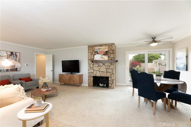 living room featuring crown molding, carpet, ceiling fan, baseboards, and a stone fireplace