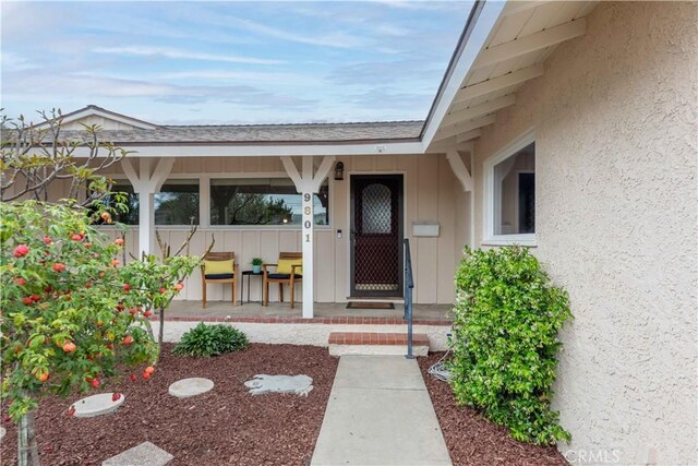 view of exterior entry with board and batten siding, covered porch, and stucco siding