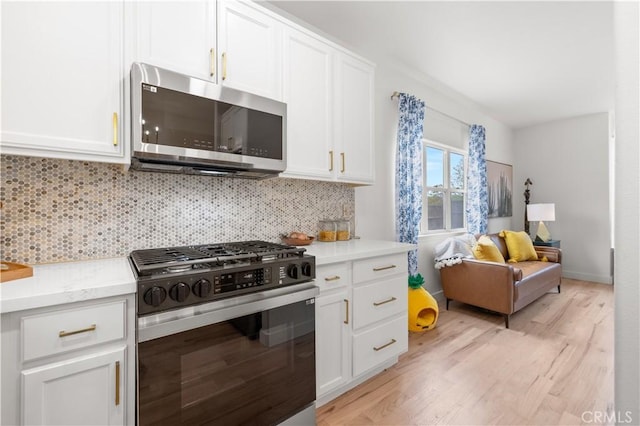 kitchen with white cabinets, stainless steel appliances, light wood-type flooring, and tasteful backsplash