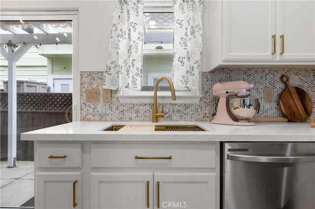 kitchen with stainless steel dishwasher, a sink, white cabinetry, and backsplash