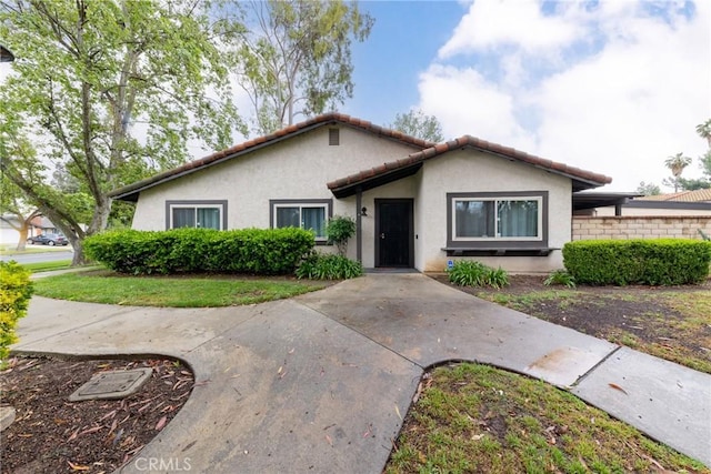 ranch-style home featuring a tiled roof, stucco siding, and fence