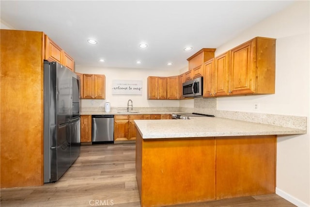 kitchen featuring stainless steel appliances, a peninsula, a sink, recessed lighting, and light wood-style floors