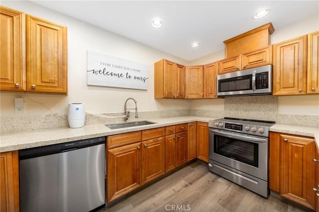 kitchen with appliances with stainless steel finishes, a sink, light wood-style floors, light stone countertops, and recessed lighting