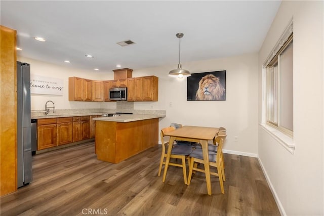 kitchen featuring appliances with stainless steel finishes, a peninsula, dark wood finished floors, brown cabinetry, and baseboards