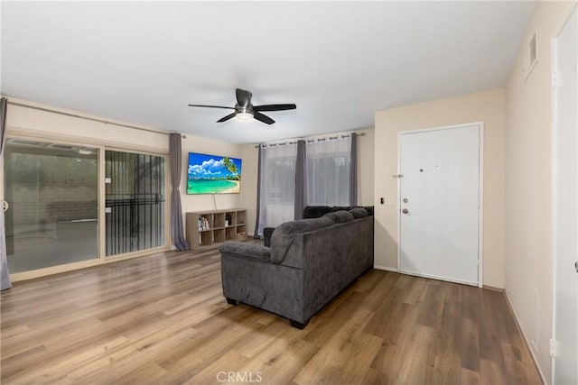 living area featuring a ceiling fan, wood finished floors, baseboards, and healthy amount of natural light