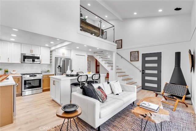 living area featuring stairs, recessed lighting, light wood-style floors, and a towering ceiling