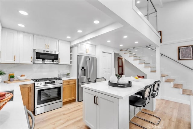 kitchen with stainless steel appliances, a breakfast bar, white cabinetry, and light wood-style flooring