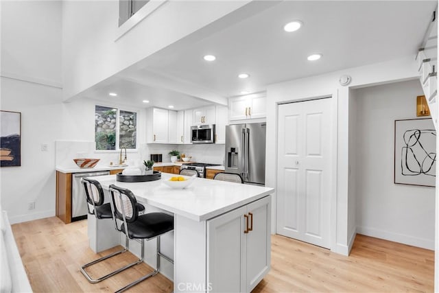 kitchen featuring a kitchen island, a kitchen bar, appliances with stainless steel finishes, a sink, and white cabinetry