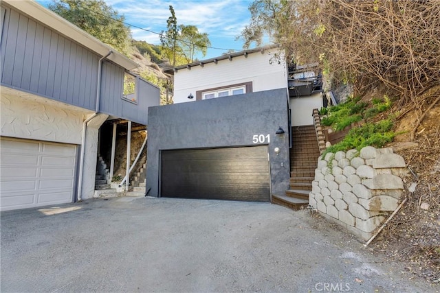 view of front of house with a garage, stucco siding, driveway, and stairway