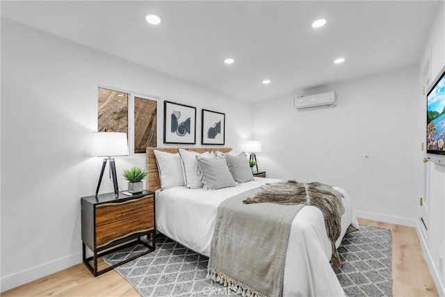 bedroom with recessed lighting, baseboards, a wall unit AC, and light wood finished floors