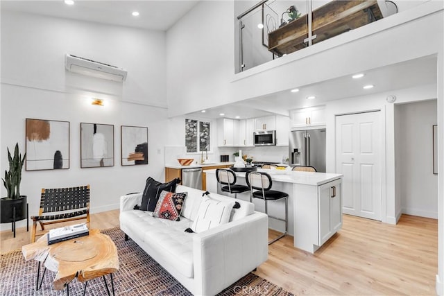 living area featuring baseboards, a high ceiling, an AC wall unit, and light wood-style flooring