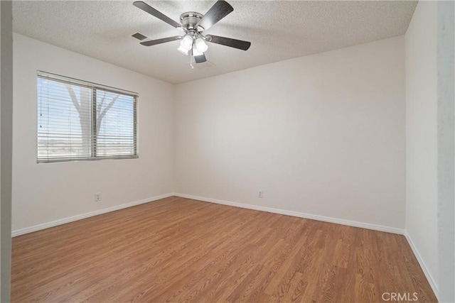spare room featuring ceiling fan, light wood finished floors, a textured ceiling, baseboards, and visible vents