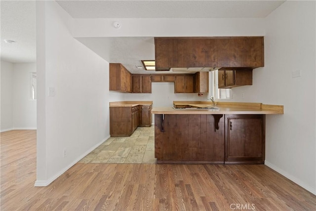 kitchen featuring light countertops, a peninsula, baseboards, and light wood finished floors